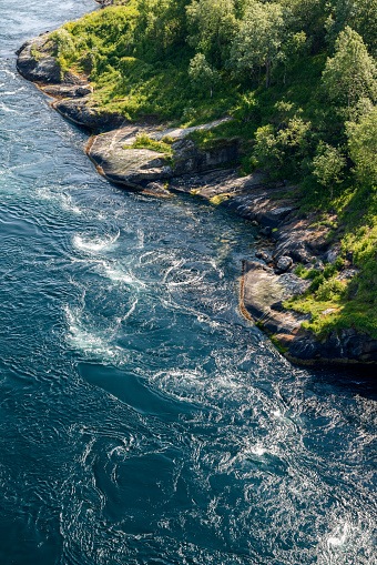 Vertical view of Saltstraumen's violent whirlpools beside the lush shoreline, a stunning display of Norway's tidal might