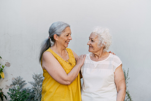 portrait of two smiling happy senior woman standing embraced in front yard