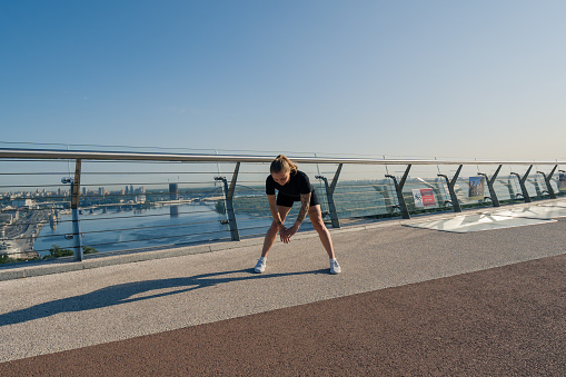 Fitness young sportswoman girl in morning doing warm-up exercises before training on the street in the city on the bridge Sport health