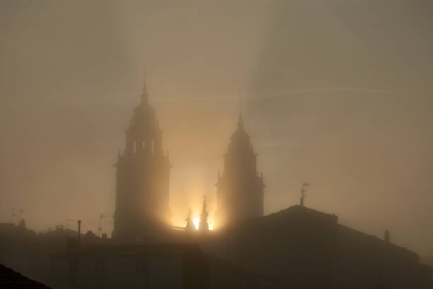 The towers of Lugo Cathedral as the sun rises in the morning on a foggy day