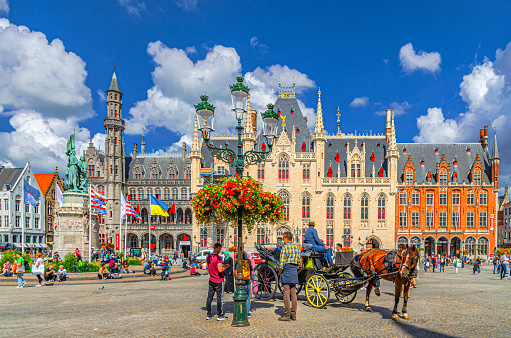 Bruges, Belgium, July 5, 2023: horse-drawn carriage cart and people tourists on Market square, Provinciaal Hof Provincial Court, Historium Bruges historical museum in Brugge old town city centre