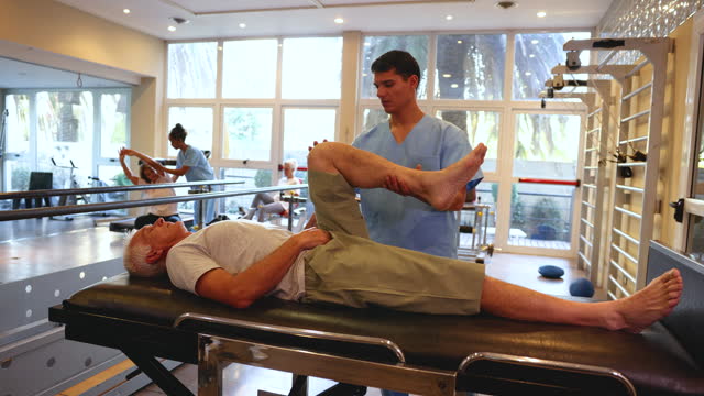 Senior patient stretching his leg with the help of male therapist during physical rehab