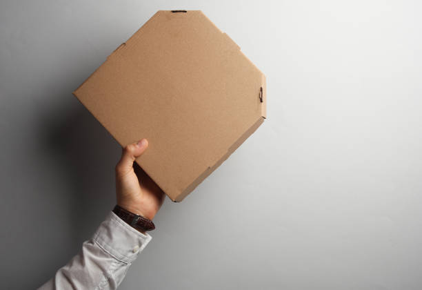 istock Man's hand in white shirt holds pizza box on gray background 1972985302