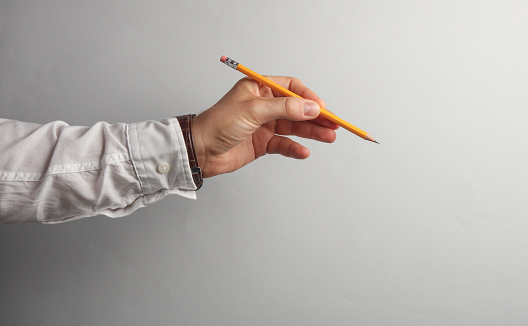 Man's hand in white shirt holds pencil on gray background. Business concept