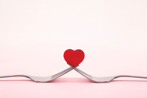 Red heart between two forks on pink background