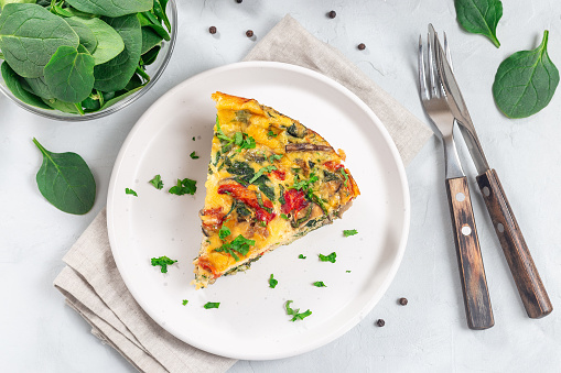 Piece of egg frittata with spinach, roasted peppers, mushrooms, cheese and herbs, horizontal, top view