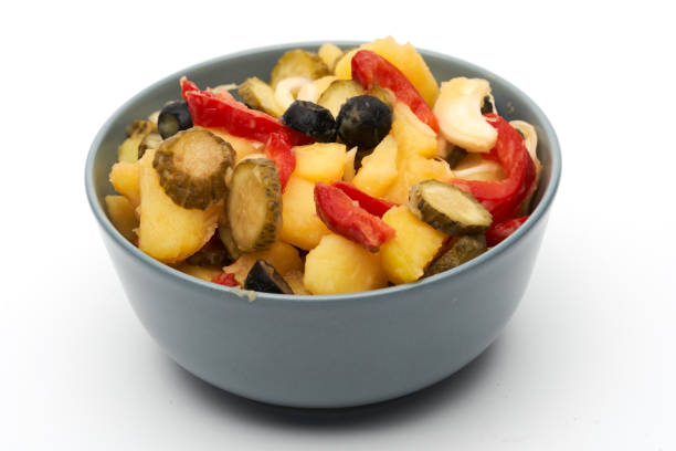 Salad of pickled olives, gherkins and peppers with potatoes in a bowl, isolated on white background