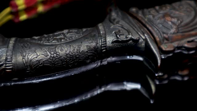 A cinematic closeup video clip of a traditional and antique Chinese knife from a low angle, while it is rotating 360 degrees with its reflection on a glass plate.