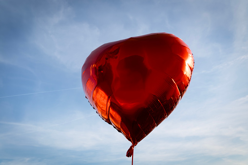 Red heart shaped and colourful air balloon flying in the sky, toned