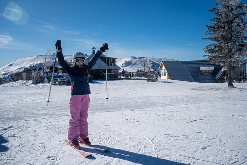 Portrait of a female skier standing on a hill and holding her skies on a snowcapped mountain ski resort.