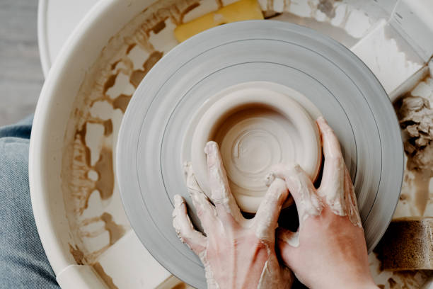 Female hands of potter forming clay product on potters wheel Female hands of a potter forming a clay product on a potter's wheel. Top view, close-up, abstract background for pottery making homemade pottery wheel stock pictures, royalty-free photos & images