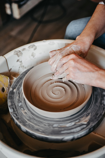 Decorating wet clay on a potter's wheel with a wine groove. A potter draws a spiral with his finger on the bottom of a white clay plate. Abstract clay background
