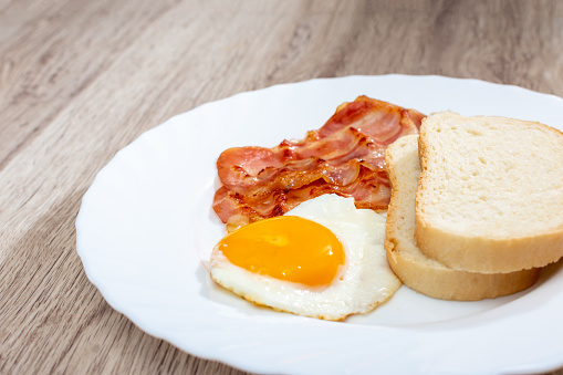 Fried bacon with egg and bread on a white plate