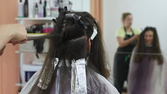 The hairdresser combs a woman's hair to apply a hair care product.