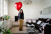 Girl holding a red heart shaped ballon in the living room of the apartment