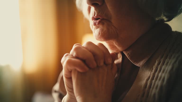 Close-up of elderly woman putting hands together, saying a prayer at home