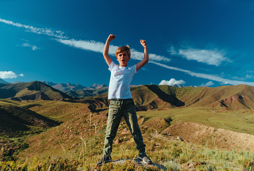 Happy boy at summer day standing in mountains in a heroic pose