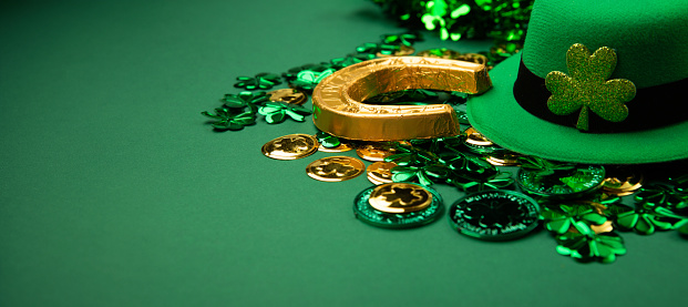 St. Patrick's Day leprechaun hat, gold coins and shamrocks on green background. Irish traditional holiday concept, copy space.