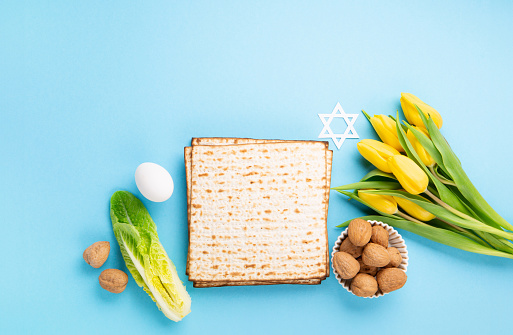 Jewish holiday Passover greeting card concept with matzah matzoh (jewish holiday bread), walnuts, yellow tulip flowers on blue table. Seder Pesach spring holiday background, copy space.