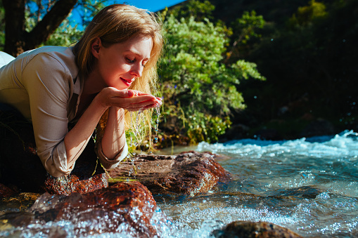 Beautiful young woman drinking water from a mountain spring