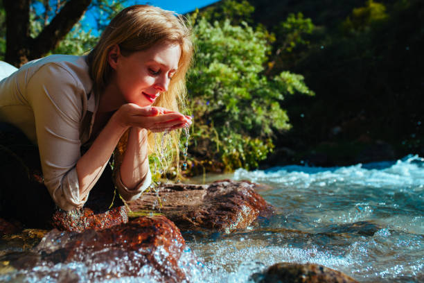 Beautiful young woman drinking water from a mountain spring stock photo