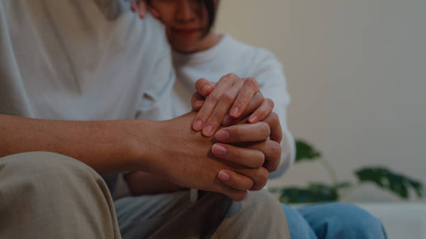 Closeup young Asian woman supporting depressed frustrated boyfriend together on sofa in living room at home night. Lifestyle spend time house. Closeup young Asian woman supporting depressed frustrated boyfriend together on sofa in living room at home night. Lifestyle spend time house concept. nervous holding hands stock pictures, royalty-free photos & images
