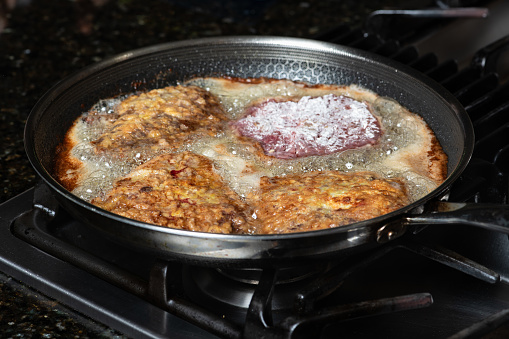 Frying schnitzel in a pan on gas cooktop. Home cooking concept.