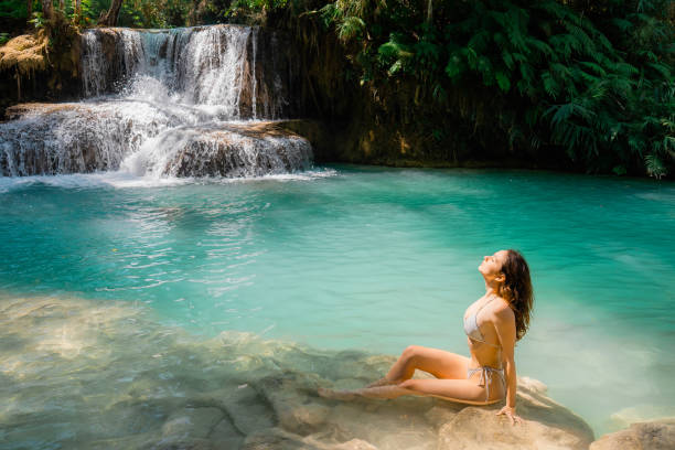 istock Woman in swimsuit  enjoys refreshing  waterfall in tropical forest 1973189374