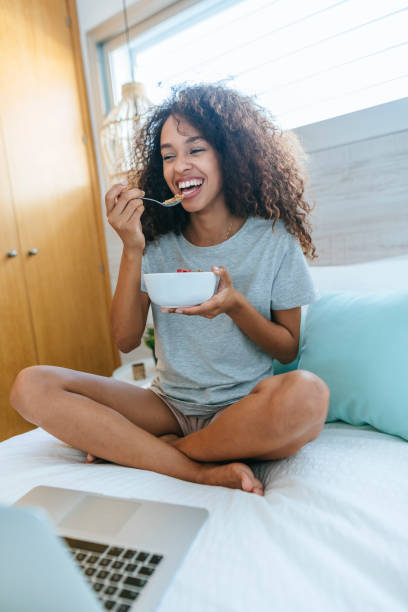istock Woman eating cereal in bed next to laptop 1973191437