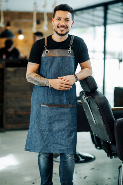 istock Smiling young barber leaning against a chair in a barber shop 1973192492