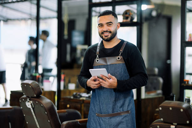 istock Smiling barber standing with a tablet in a barber shop 1973193013