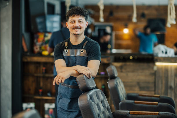 istock Young barber smiling while leaning on a chair in a barber shop 1973193014
