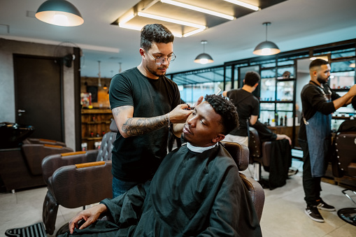 Young man barber giving a stylist haircut to male customer in modern salon