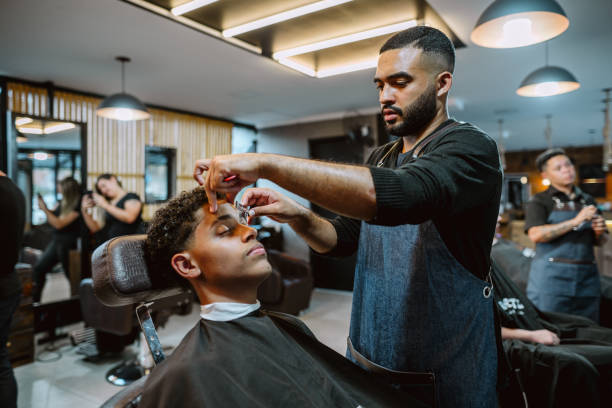 istock Barber using a razor to trim a customer's eyebrows in a barber shop 1973194118