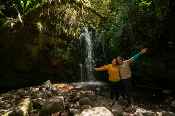istock two people standing in front of a waterfall with rocks and trees 1973197824