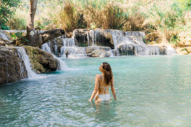 istock Woman in swimsuit  enjoys refreshing  waterfall in tropical forest 1973199384