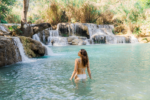 Young Caucasian woman swimming in   Kuang si waterfall in tropical forest in Southeast Asia, Laos