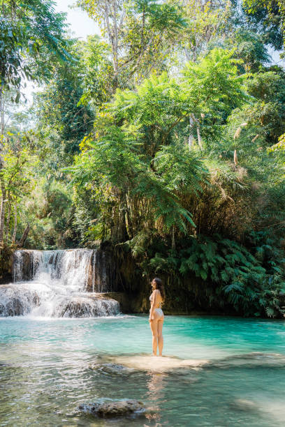 istock Woman in swimsuit  enjoys refreshing  waterfall in tropical forest 1973202021