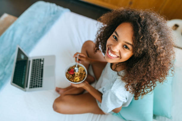 Woman eating cereal in bed next to laptop