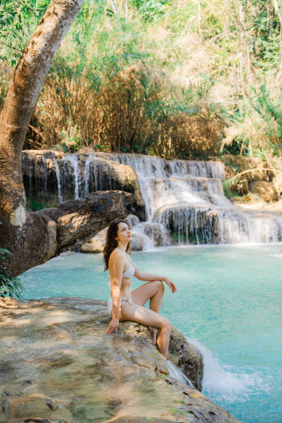 istock Woman in swimsuit  enjoys refreshing  waterfall in tropical forest 1973210491