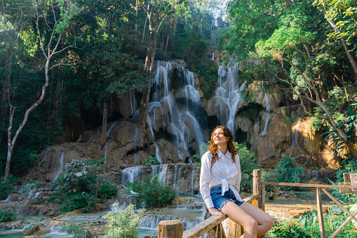 Young Caucasian woman near the waterfall in tropical forest in Southeast Asia