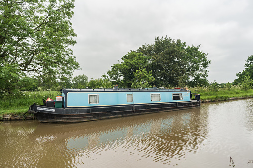Nantwich, Cheshire East, England, June 6th 2023. Vintage blue narrowboat parked on the canal, transport, travel and tourism concept illustration.
