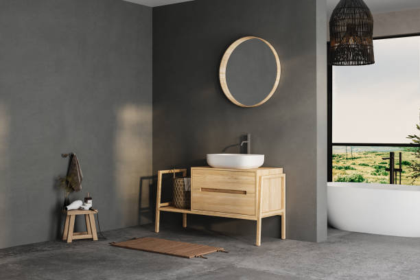 istock Modern bathroom interior with dark walls, ceramic basin with mirror, bathtub and grey concrete floor. Minimalist black bathroom with modern furniture and big windows, yard. 1973266463