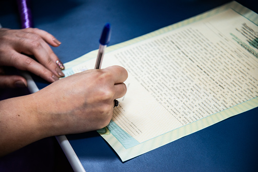 A blue pen glides across the paper as a person writes in the palm of their hand