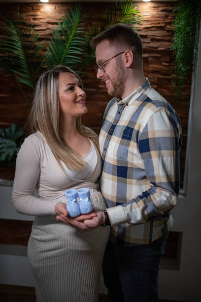 happy pregnant woman and her husband holding baby shoes - human pregnancy couple prenatal care heterosexual couple imagens e fotografias de stock