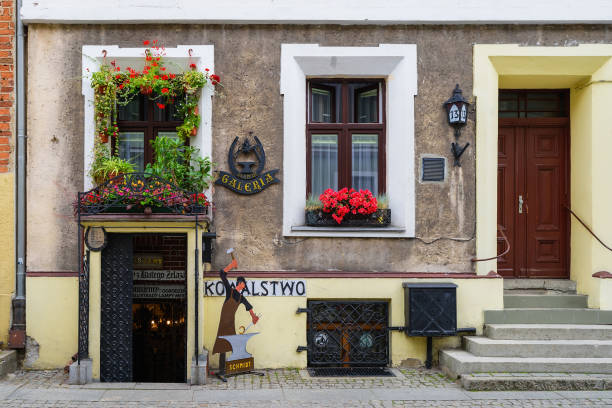 Torun, Poland - July 21, 2023: Facade decorated with colourful, blooming flowers. Building of blacksmith's gallery and workshop.  Historic facades at the famous of Torun mediaeval town.