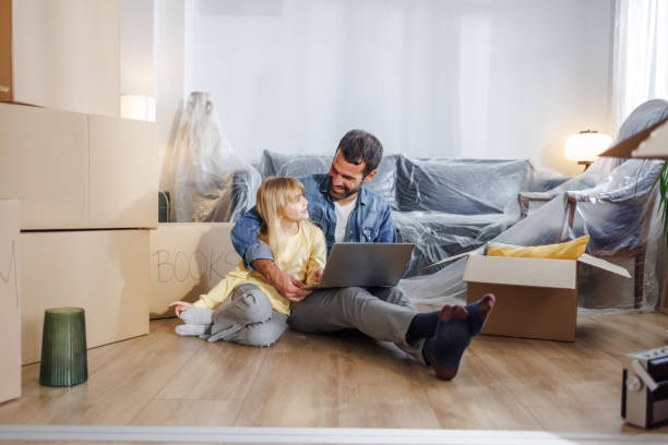 istock New homeowners - A single father arranging home moving services online with a laptop while hugging his daughter 1973293438