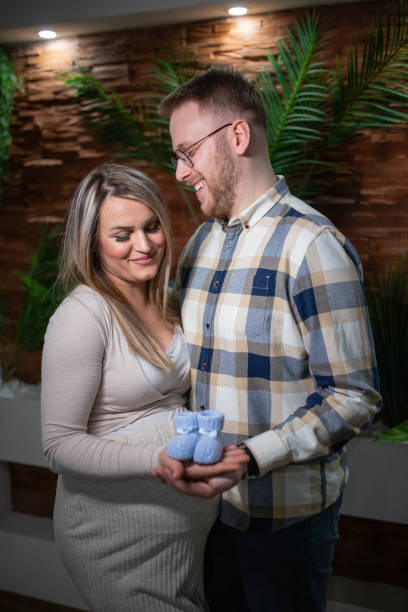 happy pregnant woman and her husband holding baby shoes - human pregnancy couple prenatal care heterosexual couple imagens e fotografias de stock