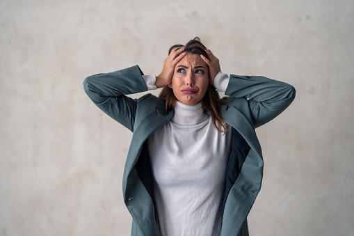 Devastated female professional holding hands on the head feeling overworked, frustration, anxiety, headache, having a problem. Worried business woman standing against studio background.