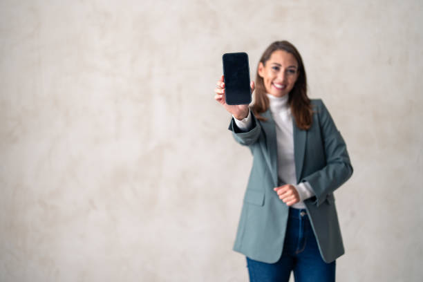 istock Smiling female showing mobile smartphone display, marketing or app on mockup 1973313334